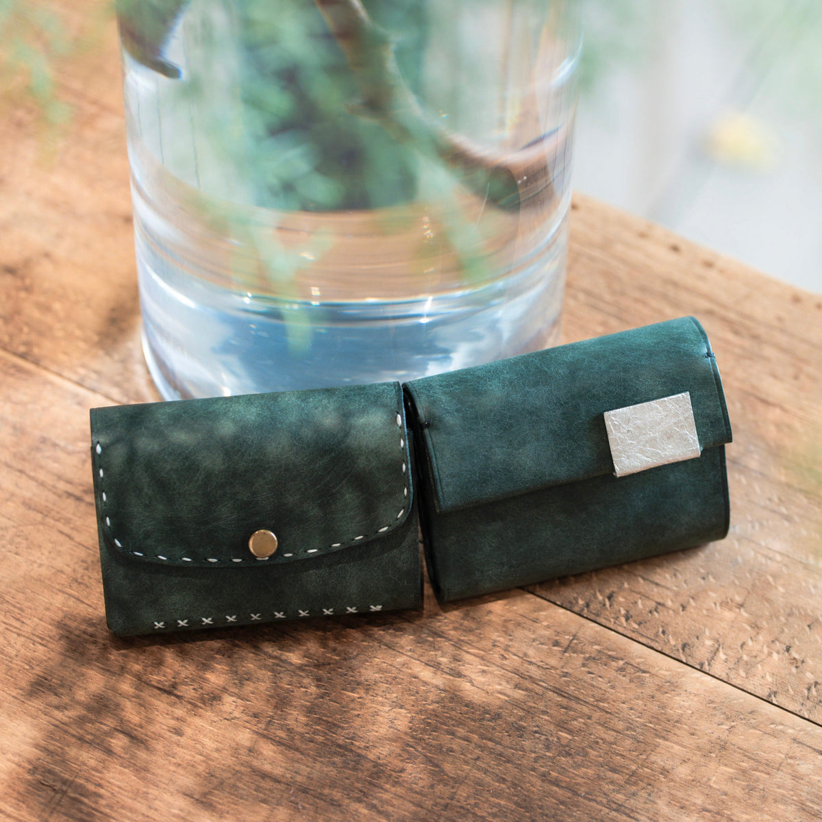 A deep green leather wallet beside glass filled with light